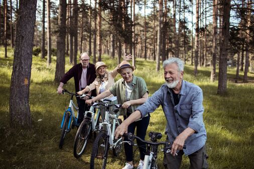 Eine Gruppe von vier Senior:innen schiebt ihre Fahrräder bei einem Ausflug durch den Wald