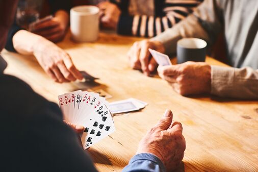 Einige Personen spielen Karten und trinken Kaffee, Fokus auf Händen und Spielkarten